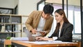 Asian businesswoman working on her tasks on a laptop while being trained by her male boss