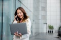 Asian businesswoman working on laptop and talking on cell phone at front building near office Royalty Free Stock Photo