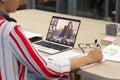 Asian businesswoman writing in diary while video conferencing with colleagues over laptop in office Royalty Free Stock Photo