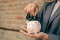 Asian businesswomen hold piggy banks and put coins in piggy banks to save money with coins to step into business, grow successful