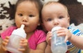 Asian and Caucasian babies laying down side by side drinking from bottles