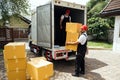 Asian and Caucasian workers in uniform unloading cardboard boxes from the truck. Delivery men unloading boxes and check. Royalty Free Stock Photo