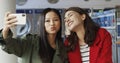 Asian and Caucasian young beautiful girls smiling and posing to smartphone camera while taking selfie photo in laundry Royalty Free Stock Photo