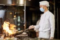 Asian chef in respiratory mask making stir-fry in flaming pan