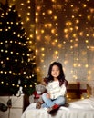 Asian child baby girl kid sitting under decorated gold Christmas tree with gold patchwork gift presents Royalty Free Stock Photo