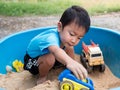 Asian child boy playing car toy in sandbox outdoor in rural nature background with smiling face. Royalty Free Stock Photo