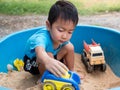 Asian child boy playing car toy in sandbox outdoor in rural nature background with smiling face. Royalty Free Stock Photo