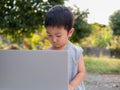 Asian child boy using notebook or laptop in rural nature background. Kid looking computer with cute face. Royalty Free Stock Photo