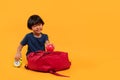 Asian child boy 3 years, Student kid smile to holding a alarm clock and apple in his hand while sitting with school bag. Isolated Royalty Free Stock Photo