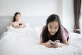 Asian child daughter using mobile phone typing text message,chatting to her mother while sit in bed together at home,addicted to a