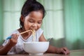 Asian child girl eating delicious instant noodles with chopsticks for her lunch in the house Royalty Free Stock Photo