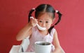 Asian child girl eating pork bone soup on high chair against red wall background at chinese restaurant Royalty Free Stock Photo