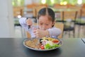 Asian child girl eating Pork steak and vegetable salad on the table with holding knife and fork. Children having breakfast Royalty Free Stock Photo