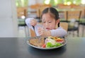 Asian child girl eating Pork steak and vegetable salad on the table with holding knife and fork. Children having breakfast Royalty Free Stock Photo