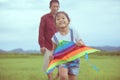 Asian child girl and father with a kite running and happy on meadow in summer in nature Royalty Free Stock Photo