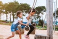 Asian child girl having fun to play on wooden swings with her sister in playground with beautiful nature