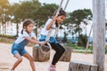 Asian child girl having fun to play on wooden swings with her sister in playground with beautiful nature