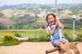 Asian child girl having fun to play on wooden swings in playground with beautiful nature