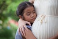 Asian child girl listening baby and hugging pregnant mother