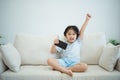 Asian child girl raise your hand cheerful success looking using and touch mobile phone screen on couch sofa. Baby smiling funny