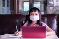 Asian child girl studying homework and wearing face mask during her online lesson at home for protect 2019-nCoV or Covid 19 Royalty Free Stock Photo