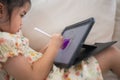 Asian child girl using pen and touch drawing on tablet display screen. Baby smiling funny time to use tablet. Too much screen time Royalty Free Stock Photo