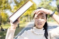 Asian child girl walking outdoor protects from the sunlight UV rays with her book,female teenager worried about hot strong sunburn Royalty Free Stock Photo