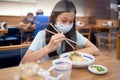 Asian child girl wear face mask with food,plastic shield as a barrier partition on the tables in restaurant during after reopening