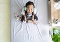 Asian child little girl play smartphone with wearing headphones on the bed Royalty Free Stock Photo