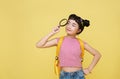 Asian child schoolgirl stood in casual wear looking at camera through magnifier while standing bright yellow background