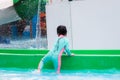 Asian children climb down the track of the slider machine. Active child wear a mint green swimsuit.