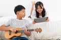 Asian children's brother and sister on the bed at home, while using laptop and playing ukulele Royalty Free Stock Photo
