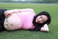 Asian Eastern Chinese happy pregnant woman lying on grass meadow in outdoor nature close eyes have a rest enjoy carefree time