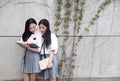 Two lovely Asian Chinese pretty girls wear student suit in school best friends smile laugh reading book in nature Royalty Free Stock Photo