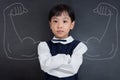 Asian Chinese girl standing against blackboard with sketched strong arms