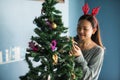 Asian Chinese happy girl with reindeer costume decorate gifts on Xmas tree. Attractive cute woman celebrate Christmas holiday in