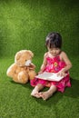 Asian Chinese little girl reading book with teddy bear Royalty Free Stock Photo