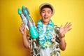 Asian chinese man wearing floral hawaian lei and water gun over isolated yellow background very happy and excited, winner Royalty Free Stock Photo