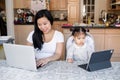 Asian Chinese mother with daughter baby working together on laptop, tablet. Workplace of freelancer woman with kid. Stay home mom Royalty Free Stock Photo