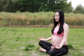 Happy smile Asian Chinese pregnant woman in yoga dress do meditation in nature sit on grass lawn live balanced healthy  life Royalty Free Stock Photo