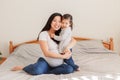 Asian Chinese pregnant woman with toddler girl hugging on bed at home. Girl daughter kid playing with mom. Mother and baby