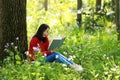 Beautiful young girl reading book while sitting under giant oak