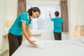 asian cleaning lady in turquoise uniform putting towel on bed