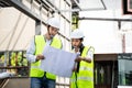 Asian Colleagues worker Specialists team wearing protective safety helmet look at blueprint on Construction Site. Civil Engineer M