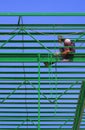 Asian construction worker is welding green metal roof industrial building structure against blue clear sky background