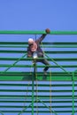 Asian construction worker is welding green metal roof industrial building structure against blue clear sky