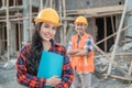Asian construction worker woman smiles at the camera wearing a safety helmet against the background of a male contractor Royalty Free Stock Photo