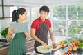 Asian couple are cooking in the kitchen. Man and Woman smiling looking menu from tablet. Man are cutting vegetables with knives. p Royalty Free Stock Photo