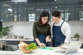 Asian Couple cooking together in home kitchen. Female slice vegetables and cooking with laptop computer. Young couples are helping Royalty Free Stock Photo