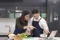 Asian Couple cooking together in home kitchen. Female slice vegetables and cooking with laptop computer. Young couples are helping Royalty Free Stock Photo